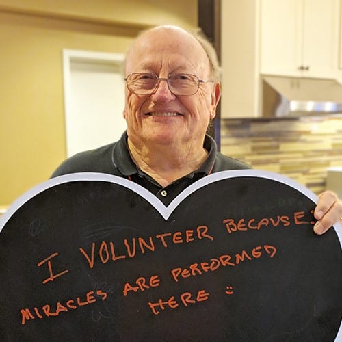 Older man smiles and holds a chalkboard that reads 
