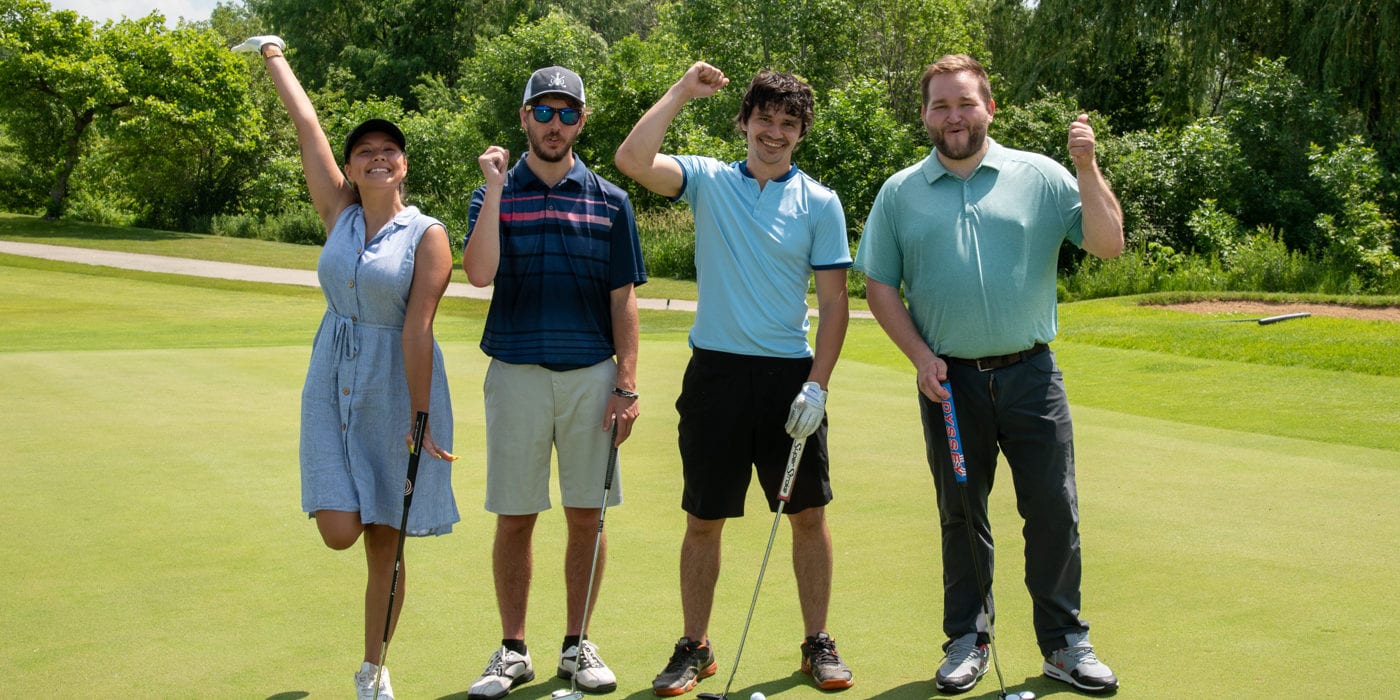 Three men and a woman stand with golf clubs and raise their fists to cheer.