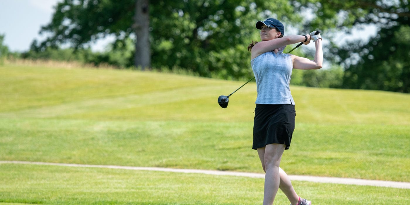 A white woman swings a golf club.