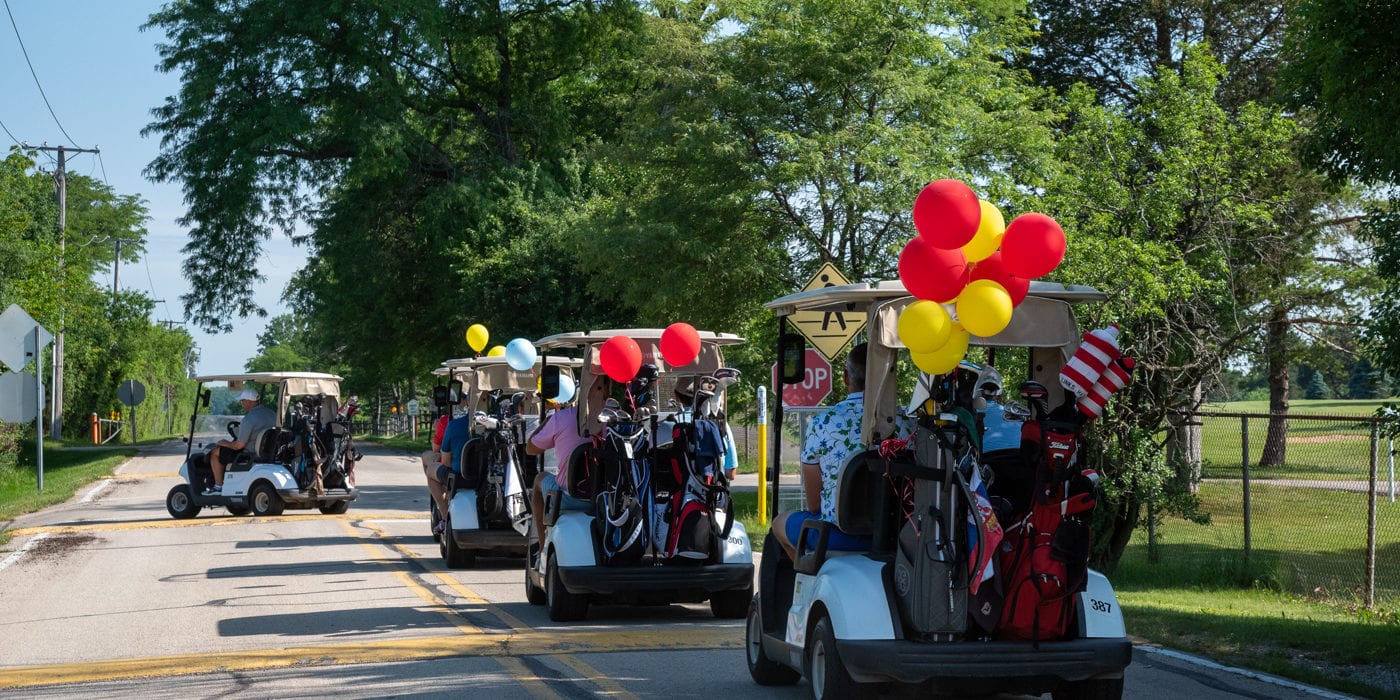 Parade of golf carts with red and yellow balloons