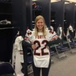 Blond woman stands in a football locker room and hold up a Chicago Bears jersey.