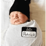 Newborn baby wrapped ina white blanket with a black hat and a "Hello, my name is Patrick" sticker.
