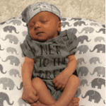 Newborn baby in a grey onesie and grey hat.