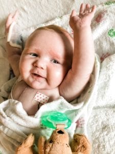 Baby in a hospital bed smiles and raises her arms
