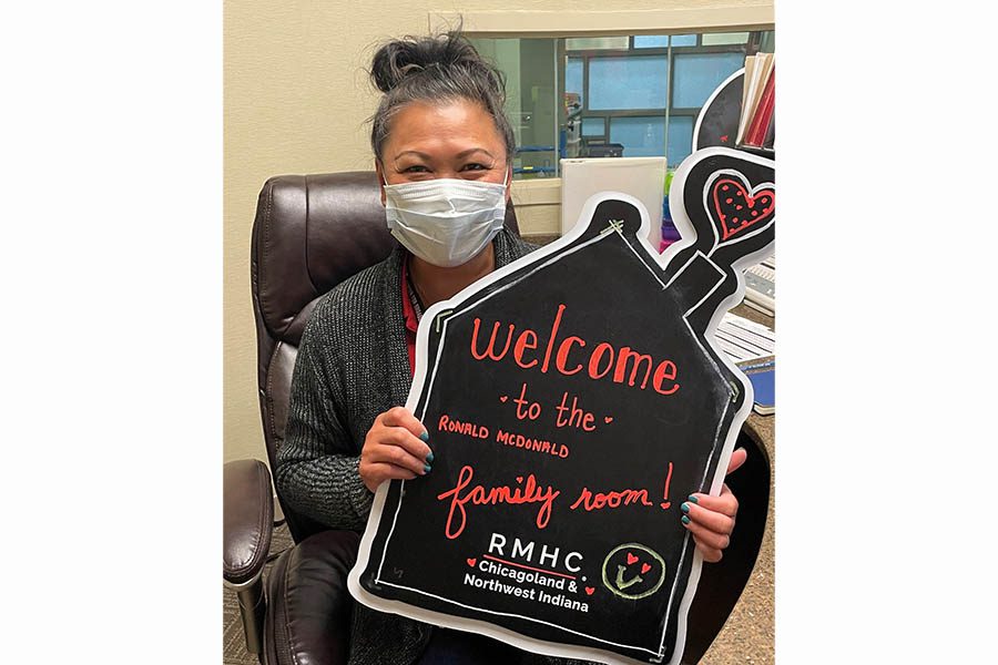 An Asian woman wearing a facemask holds a sign that reads "Wecome to the Edward Hospital Family Room!"