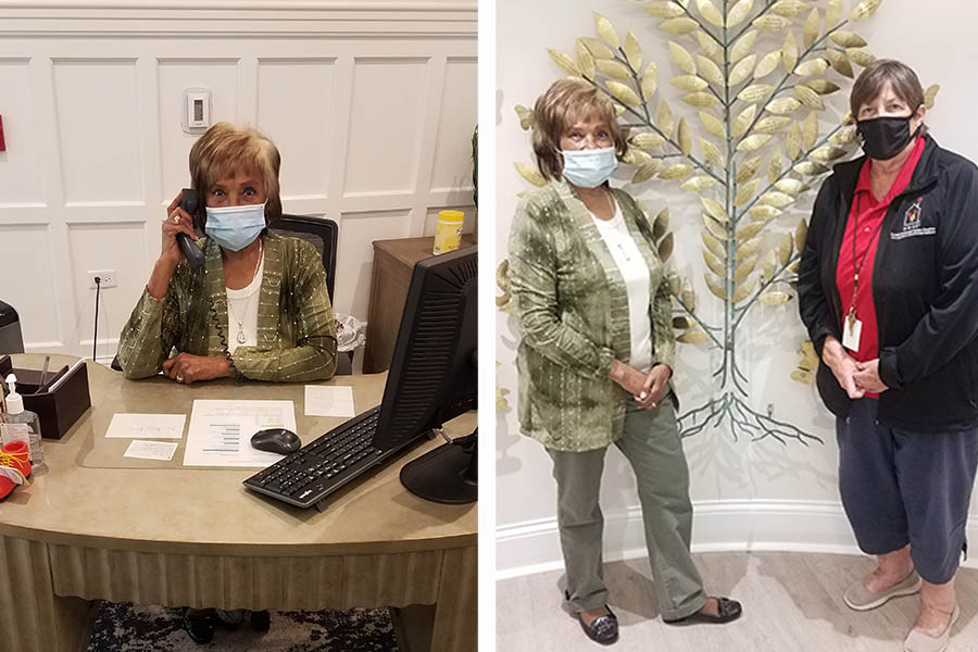 A black woman sits at a front desk answering a phone wearing a medical mask.