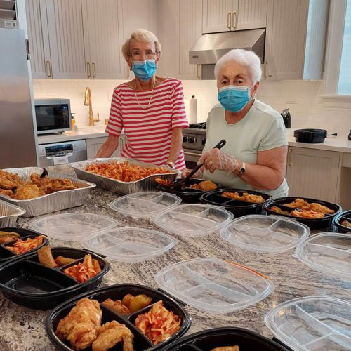 Two women stand behind a counter full of boxes of prepared meals.