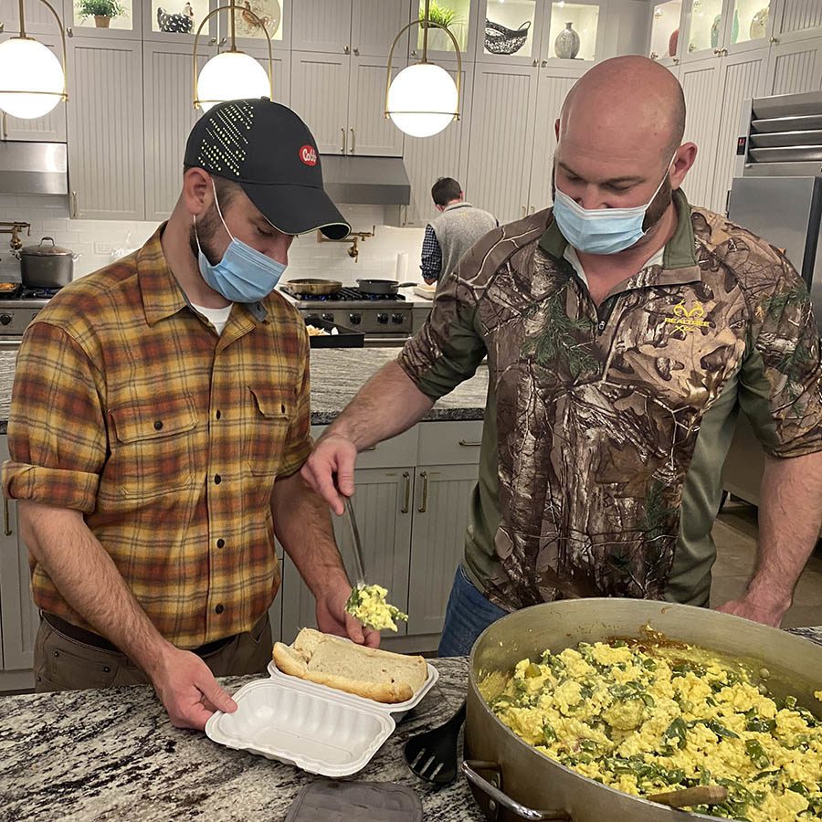 Two men stand at a kitchen counter plating prepared meals.