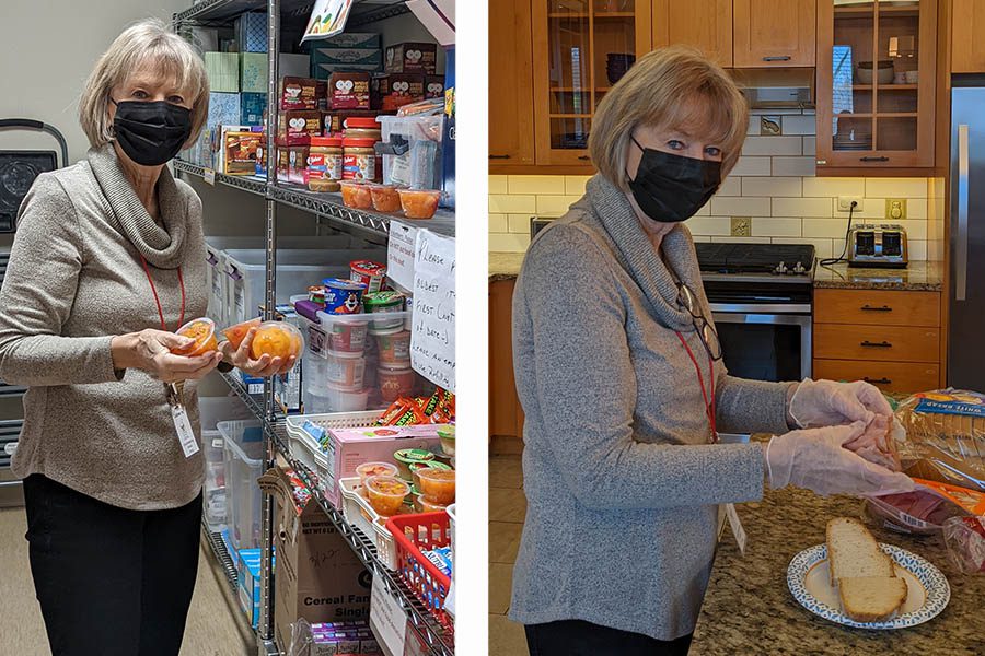 A woman with grey hair and wearing a black medical mask stands in a kitchen making a sandwich.