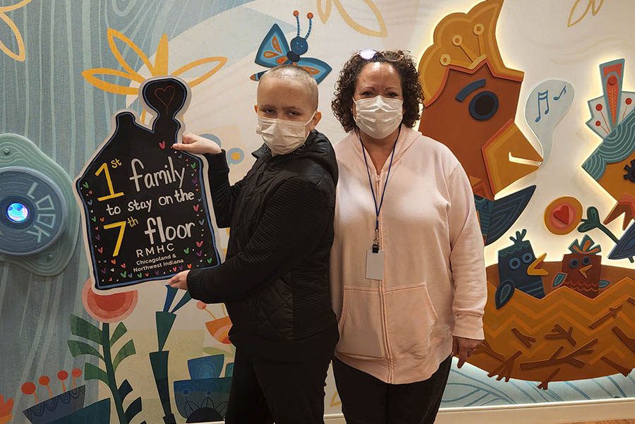 A mother and daughter stand in front of a colorful mural holding a sign that reads "1st family to stay on the 7th floor"