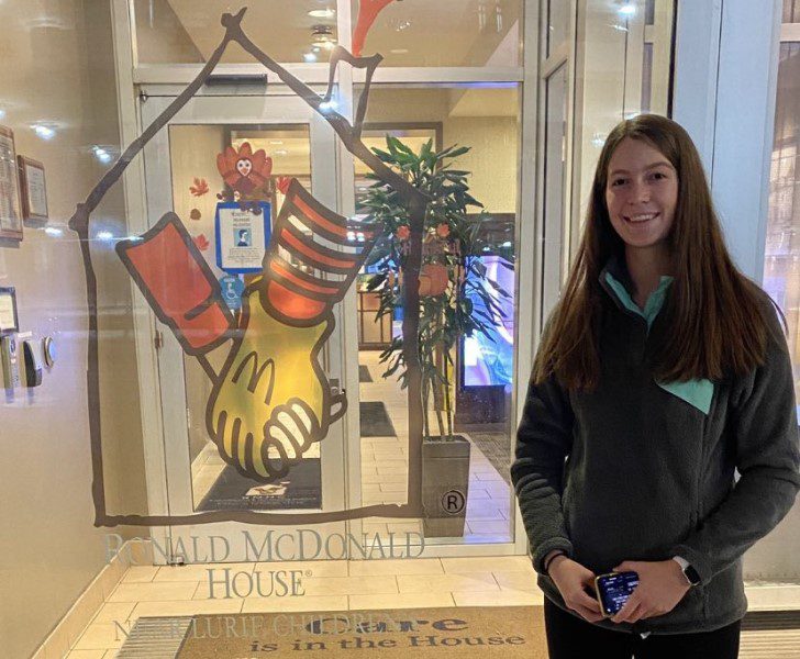 A young woman stands next to a glass window with the Ronald McDonald House logo